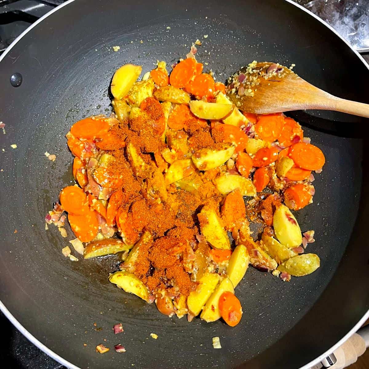 Potatoes, carrots and spices added to onions in wok.