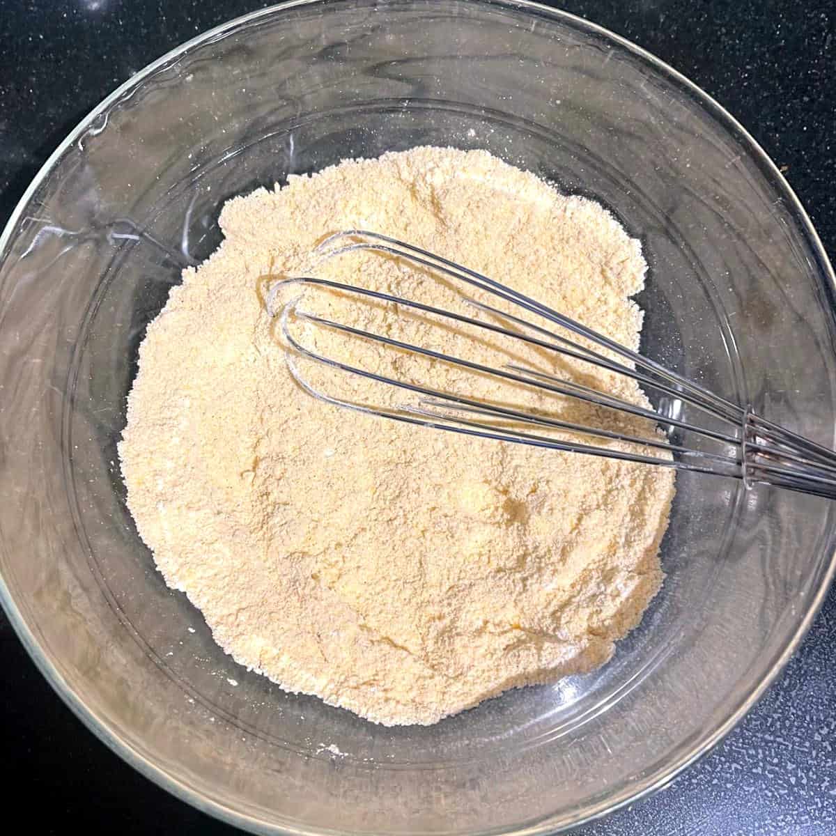 Dry ingredients in glass bowl with whisk.