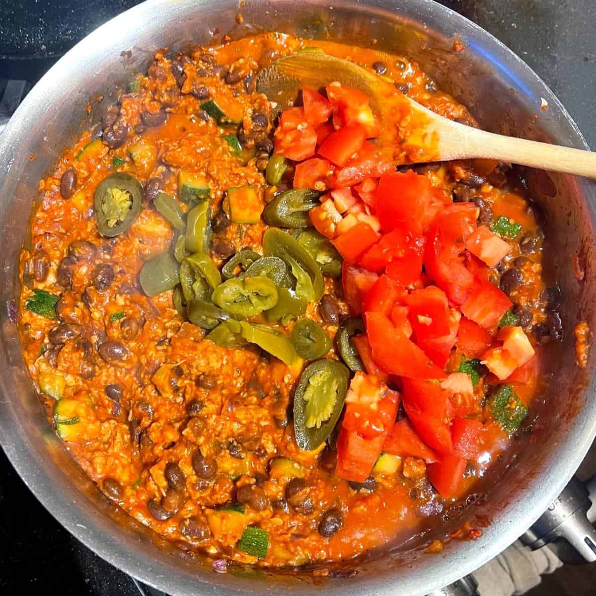 Tomatoes and jalapeno peppers added to chili in saucepan.