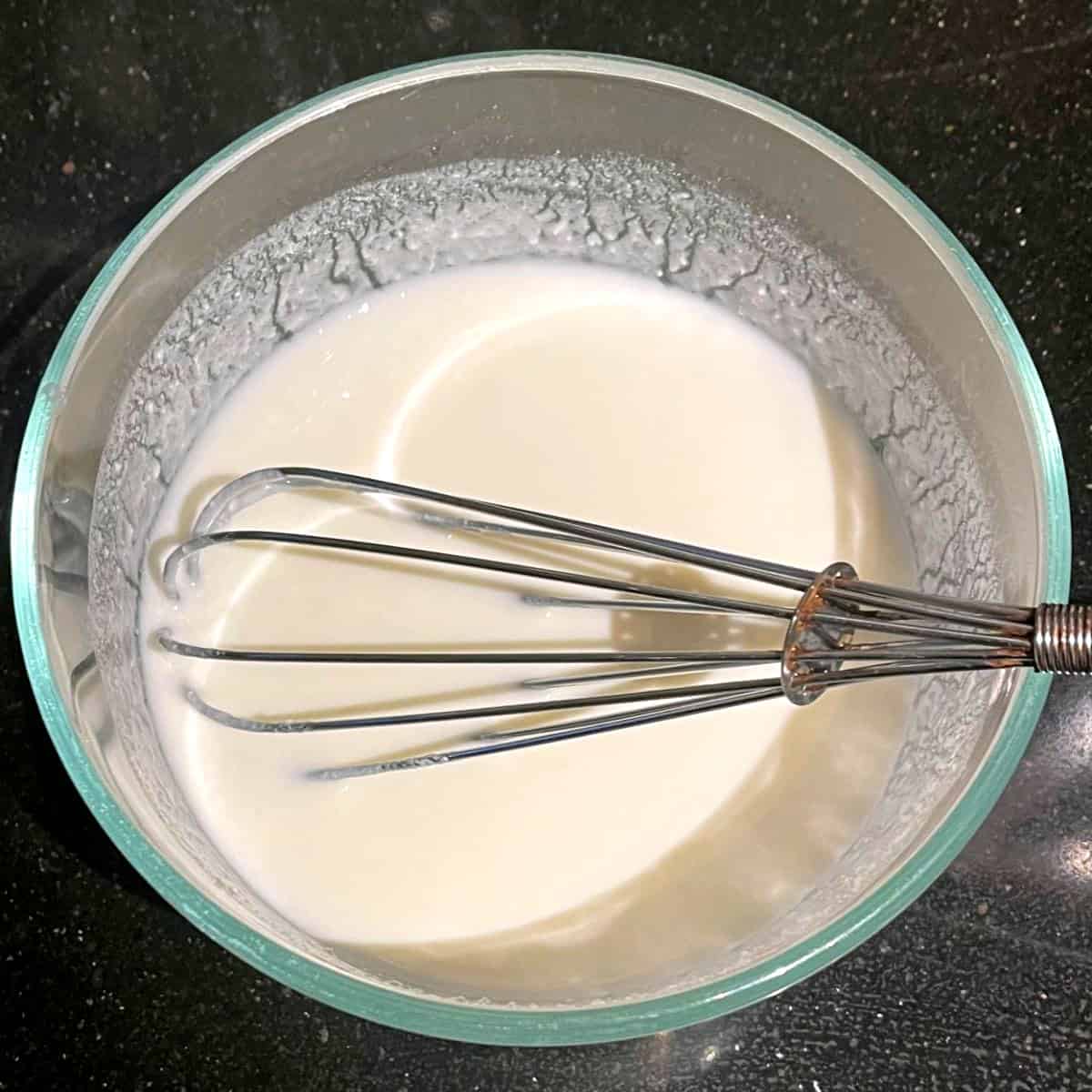 Vegan yogurt whisked with water in bowl.