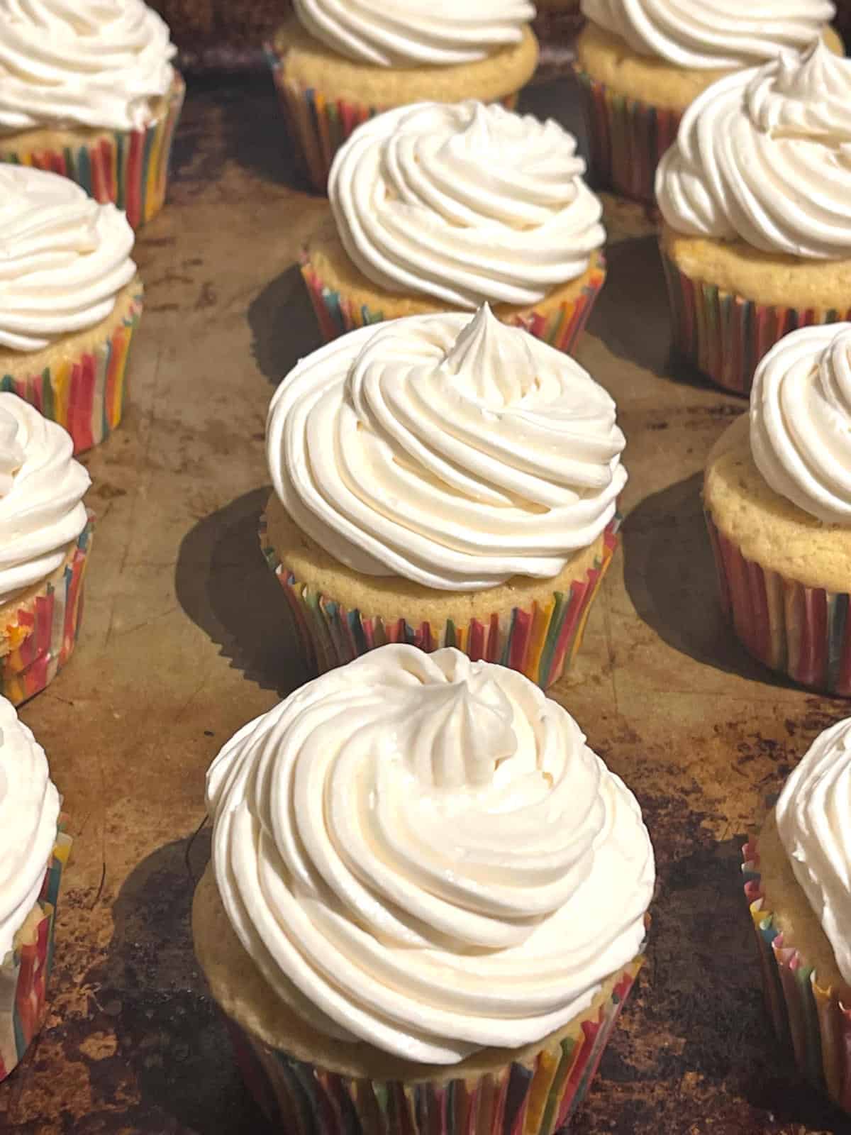 Frosted vegan vanilla cupcakes on baking sheet.