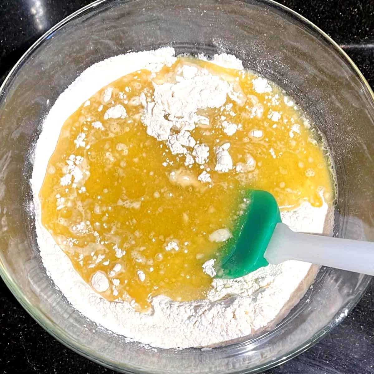 Dry and wet ingredients for vanilla cupcakes in bowl with spatula.