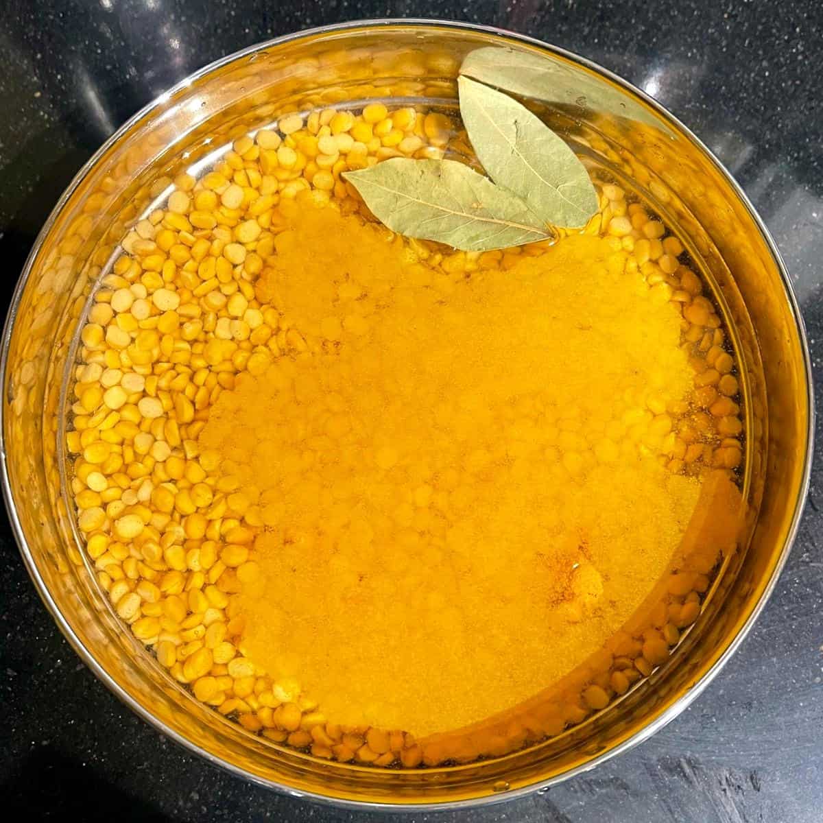 Chana dal with water, bay leaves and turmeric, before cooking.