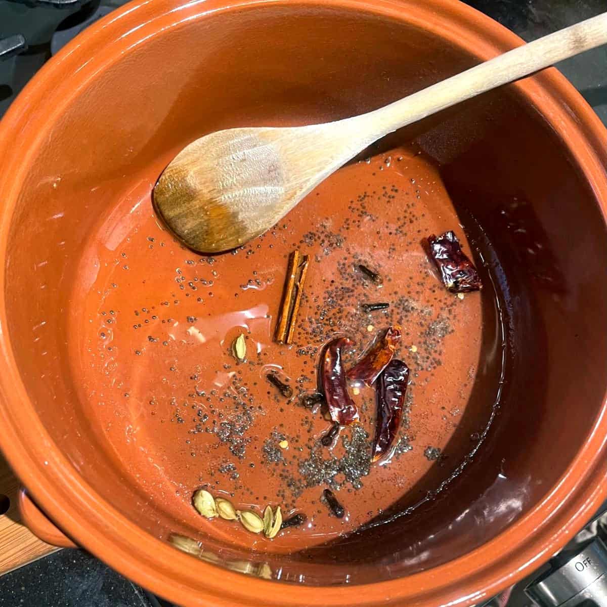 Spices sauteing in oil in clay dutch oven.