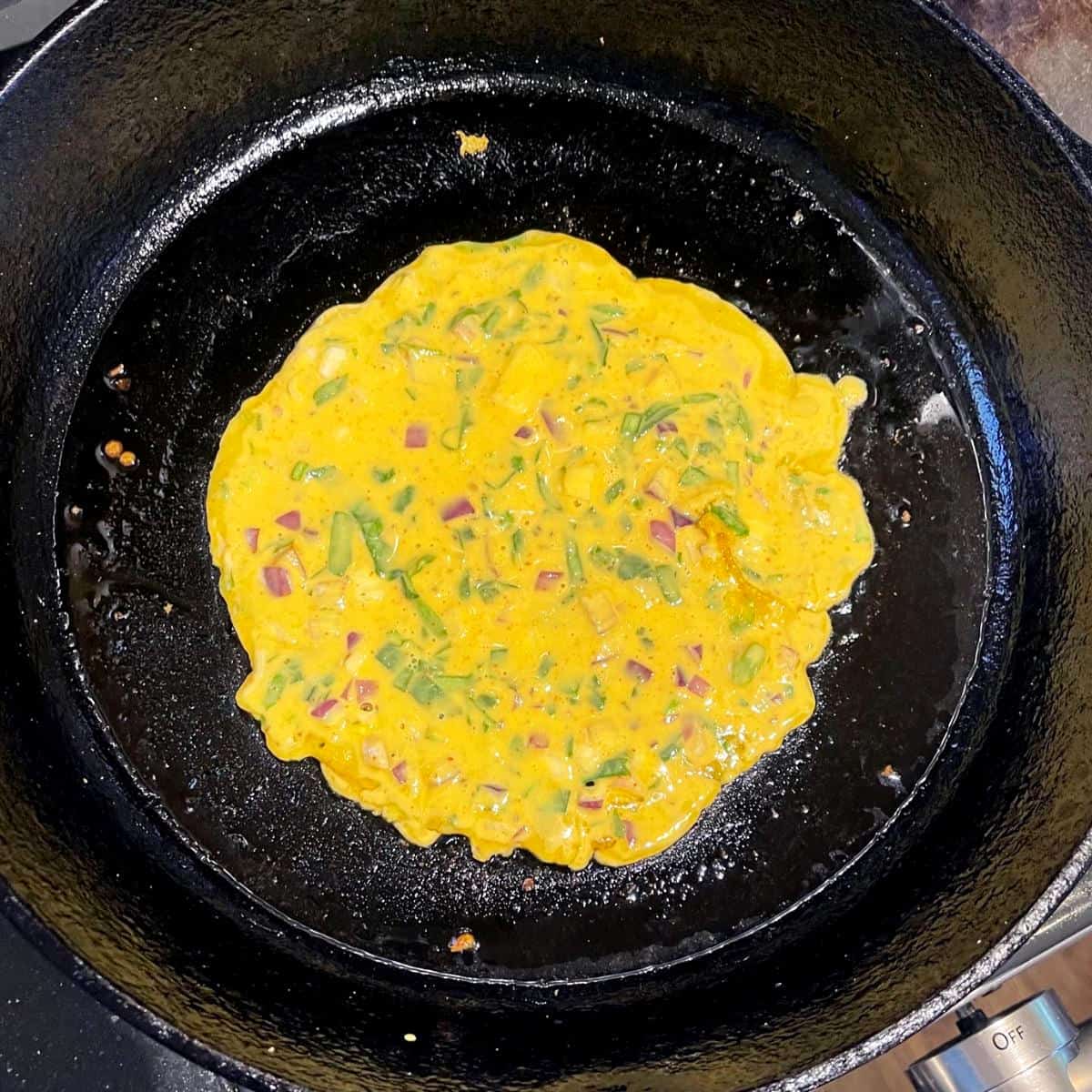Besan chilla cooking on cast iron skillet.