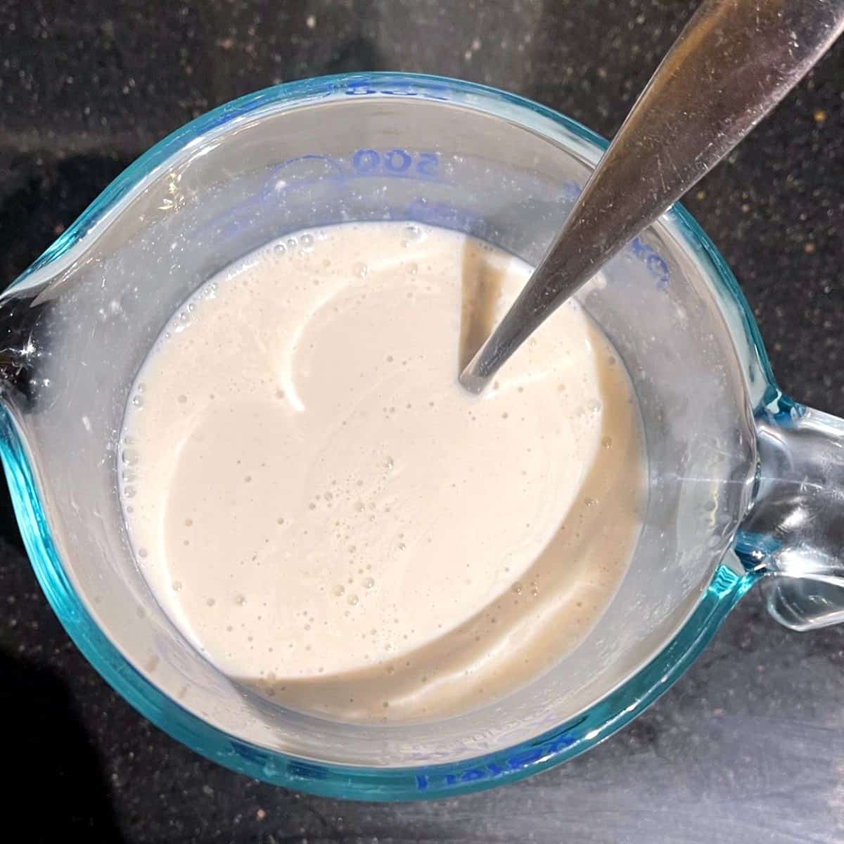Vegan buttermilk in cup measure with spoon.