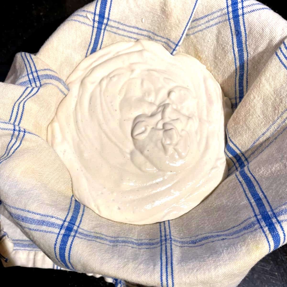 Vegan yogurt in strainer lined with kitchen towel.