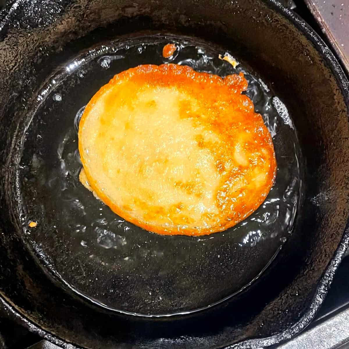 Vegan malpua frying to golden-brown color in cast iron skillet.
