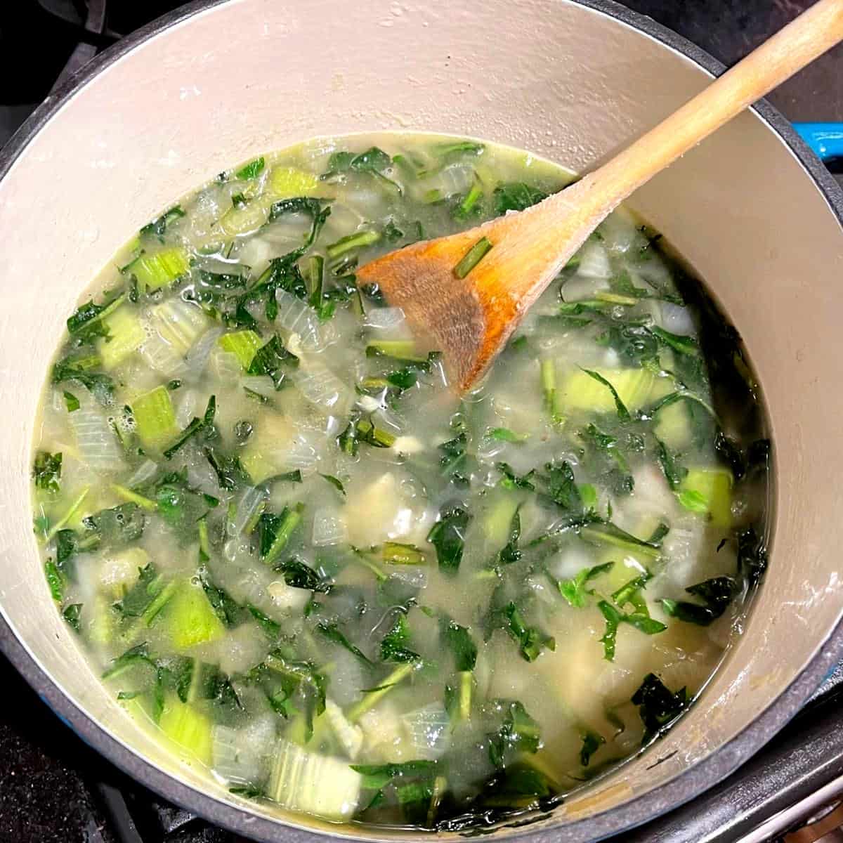Water added to dandelion greens, onions and celery in Dutch oven.