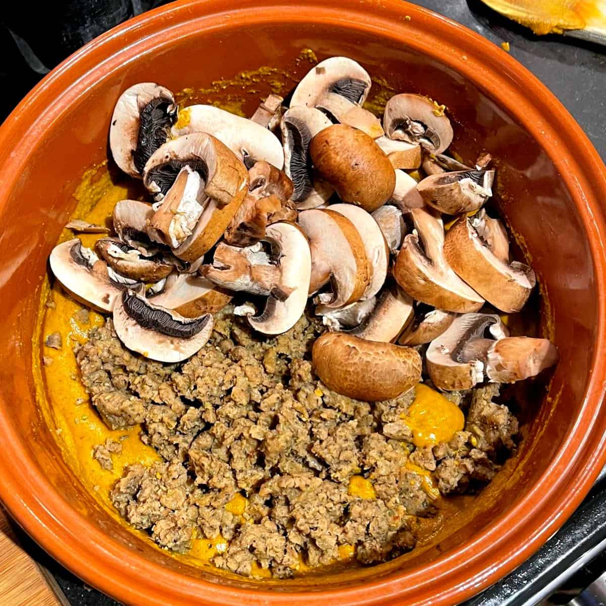 Mushrooms and seitan crumbles added to curry paste in pot.