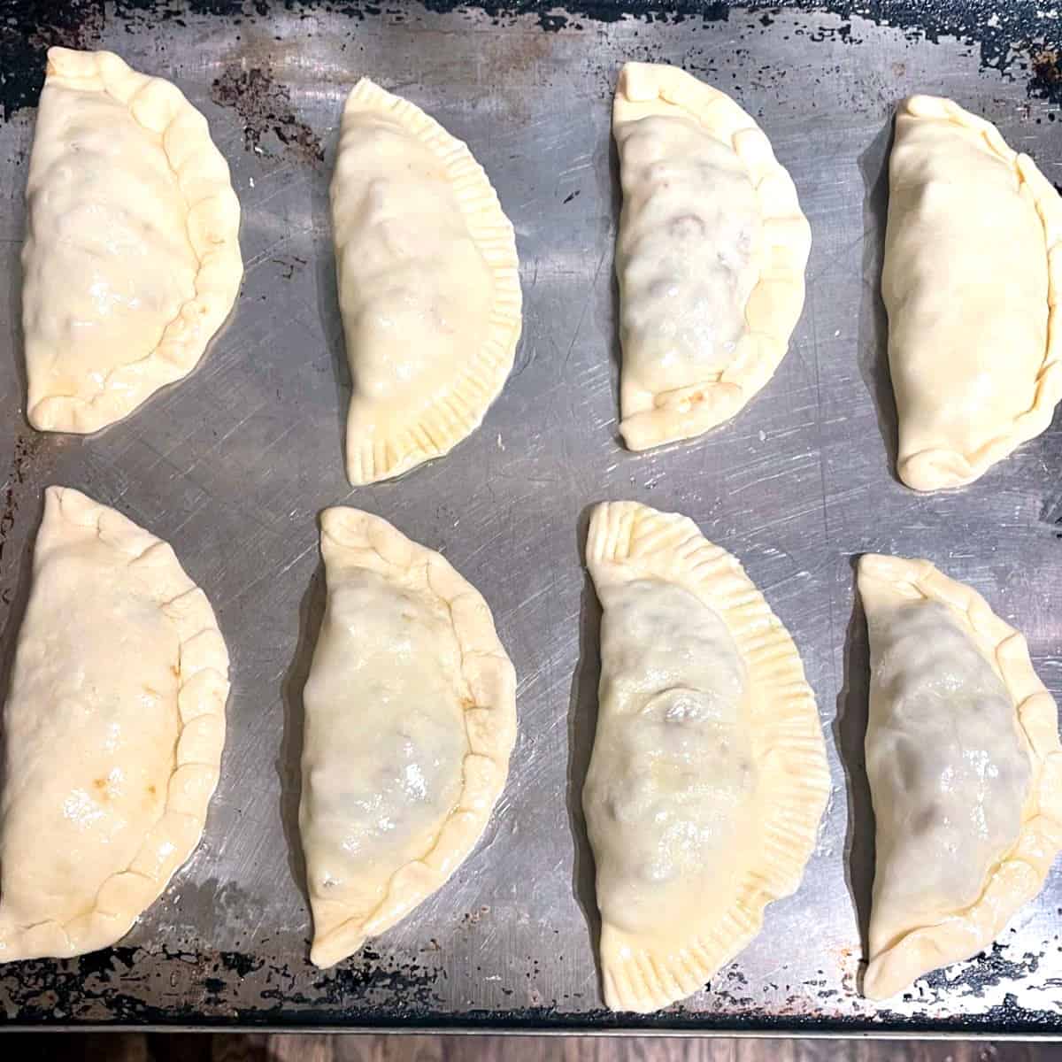 Vegan empanadas on baking sheet ready to go into oven.