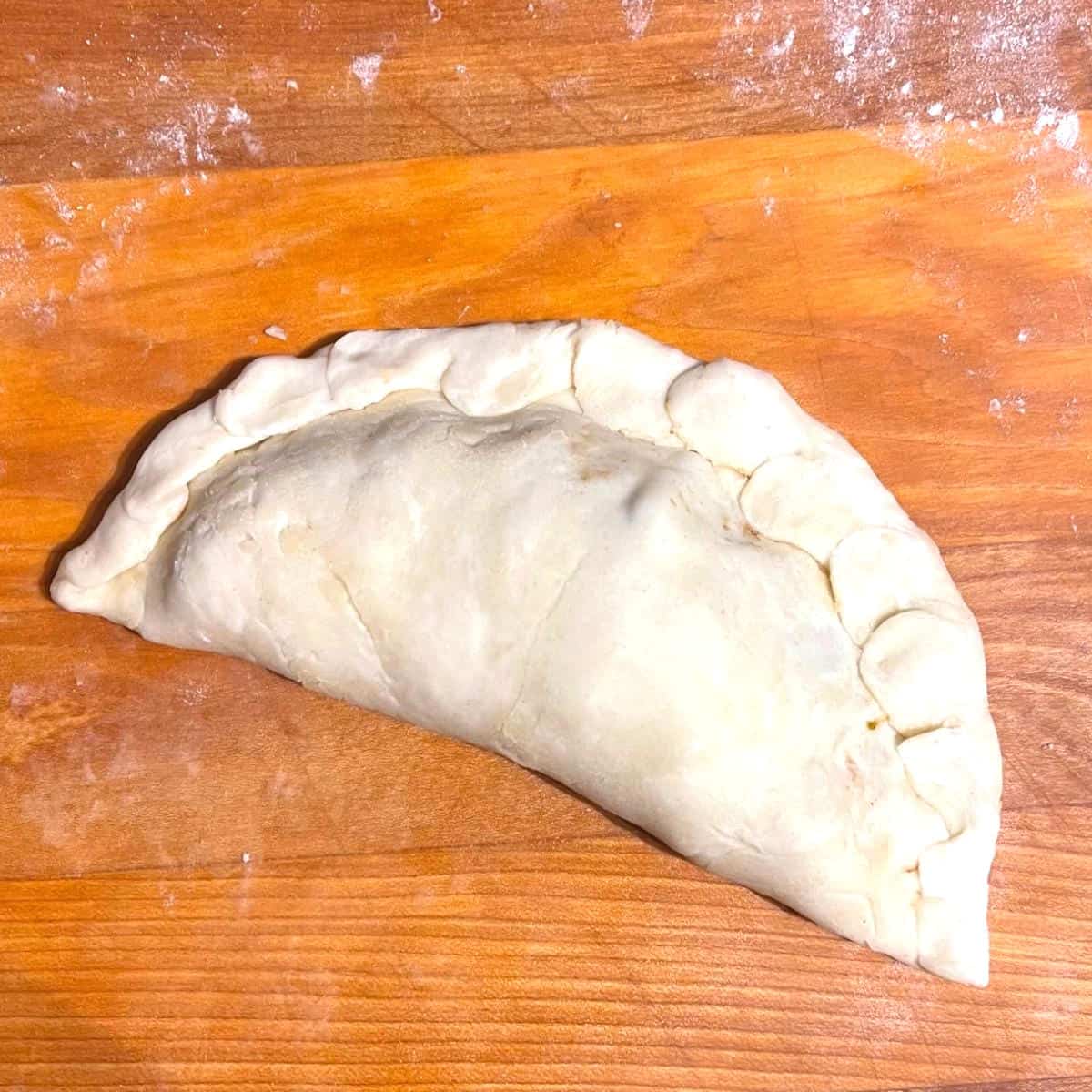Shaped vegan empanada with crimped edges.