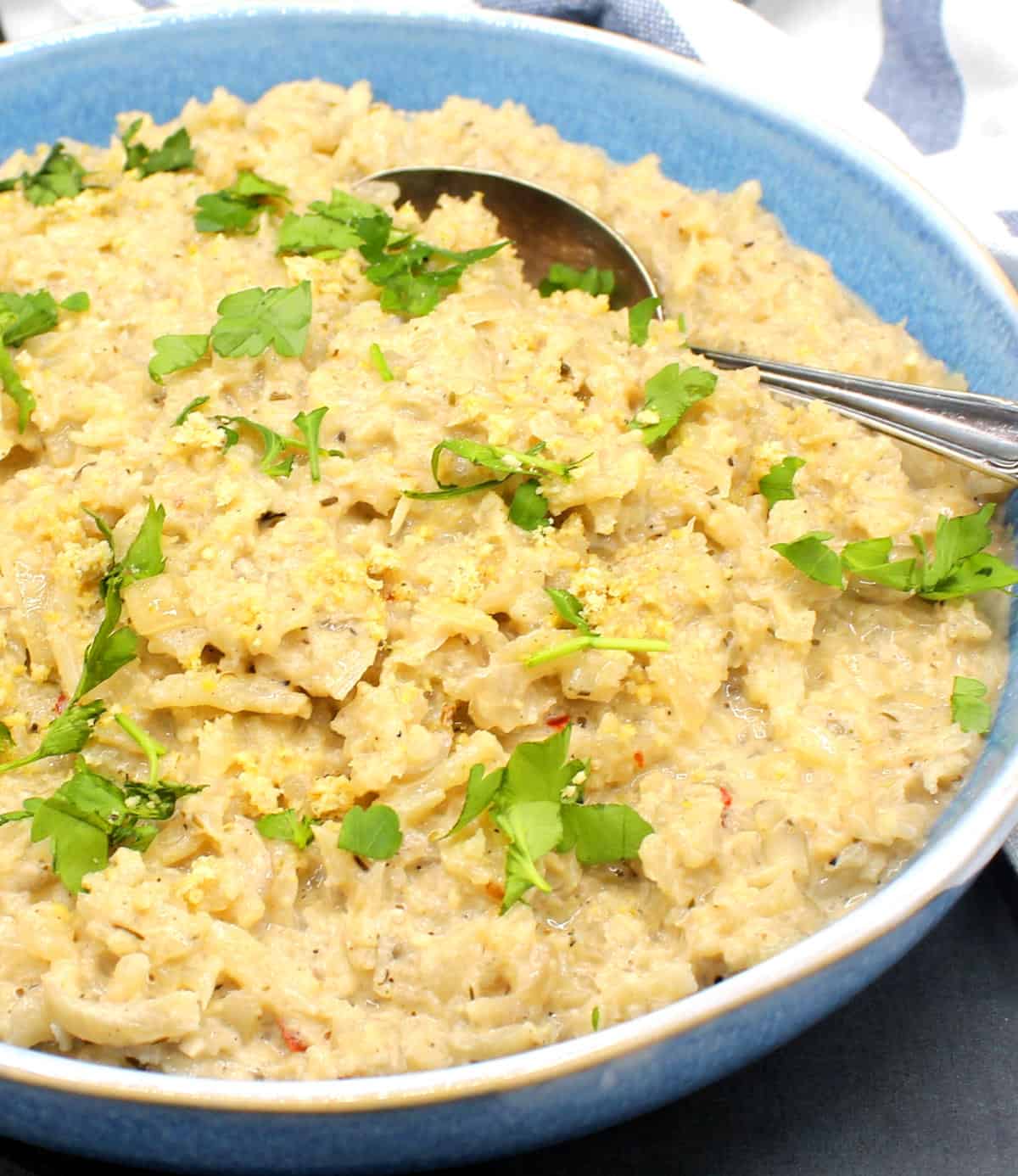 Creamy cauliflower risotto in blue bowl with spoon.