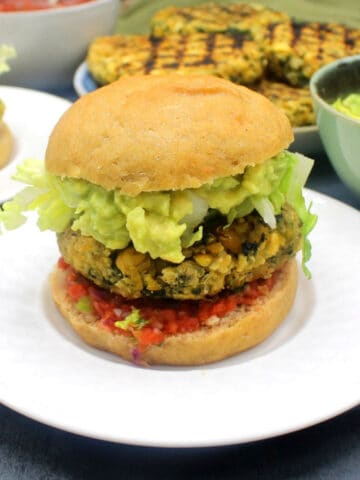 Chickpea quinoa burgers on white plates with toppings in background.