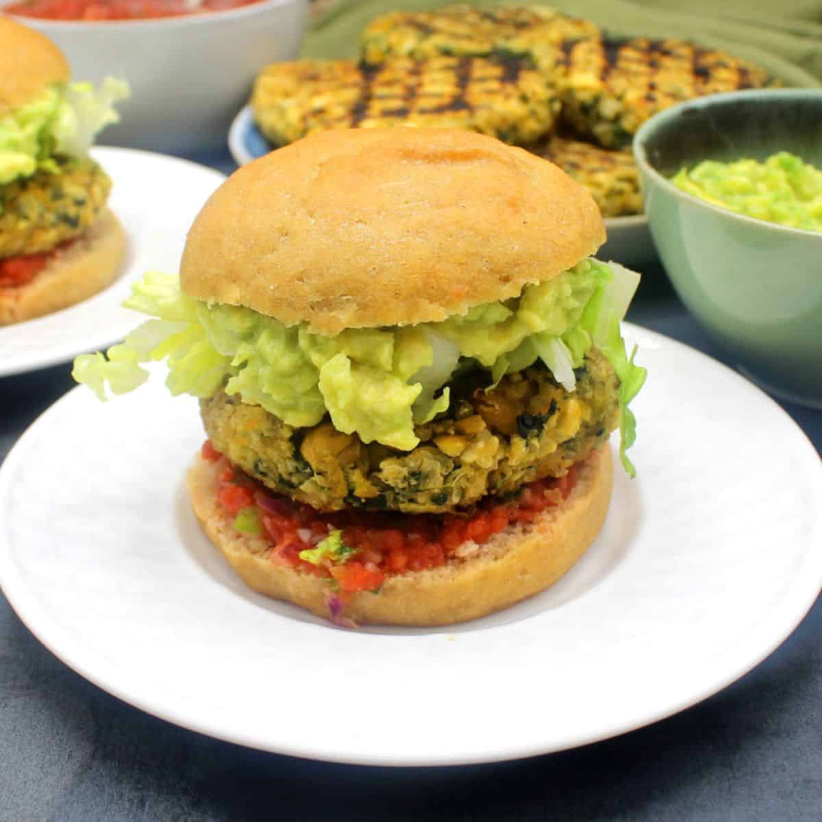 Chickpea quinoa burgers on white plates with toppings in background.