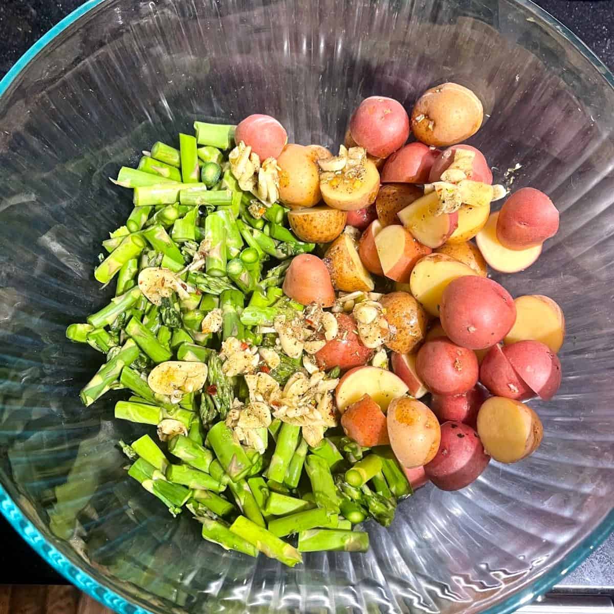 Olive oil dressing added to asparagus and potatoes in bowl.