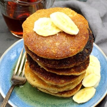 Stack of pancakes on blue plate with banana slices and maple syrup.