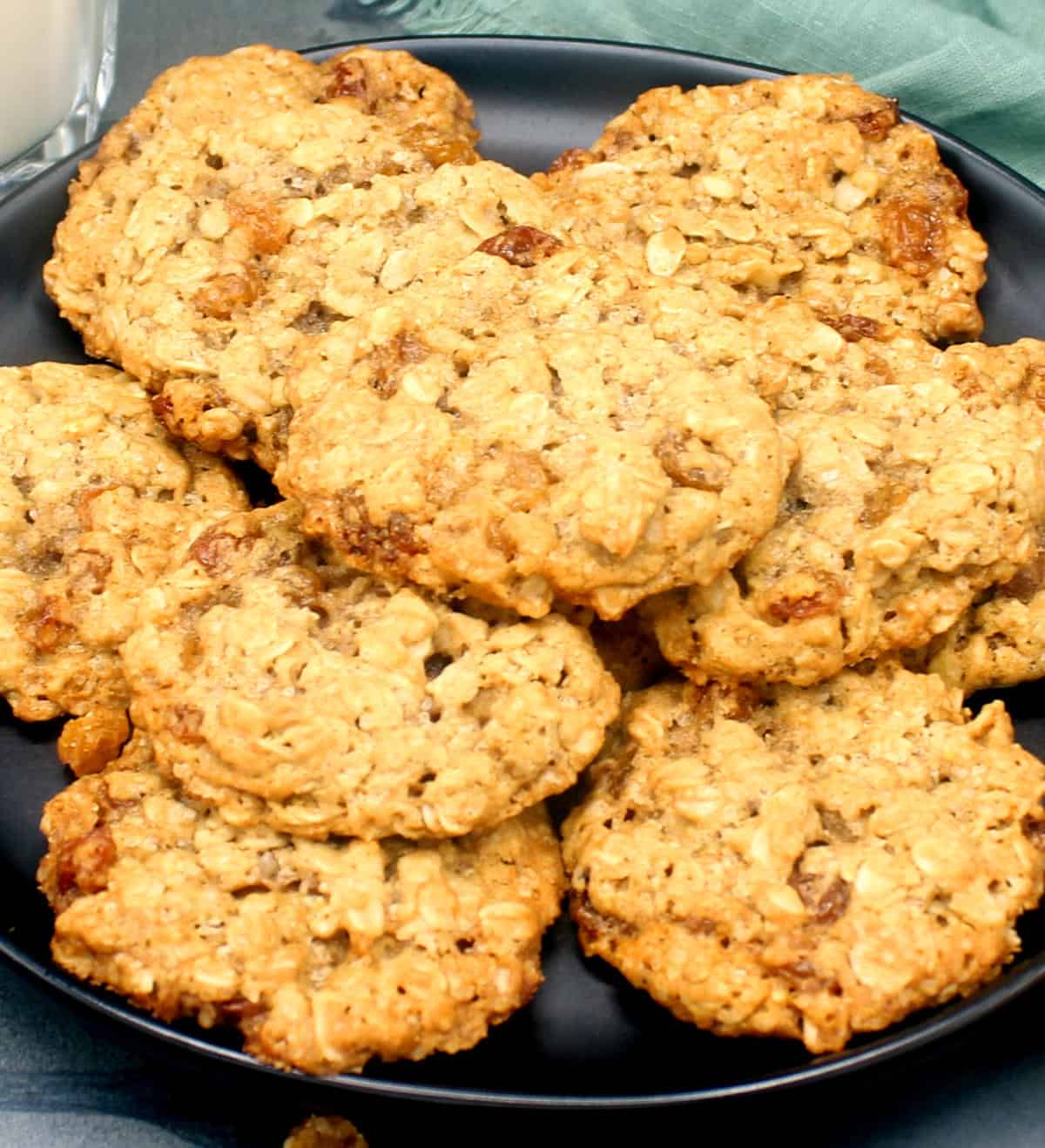 Vegan oatmeal raisin cookies piled on a black plate.