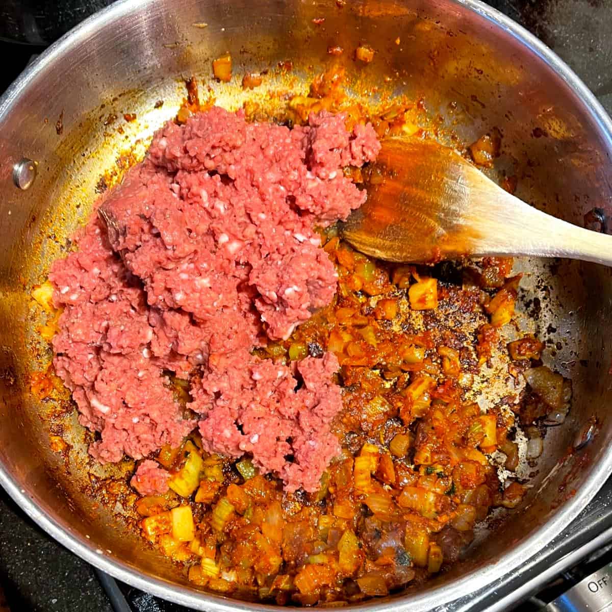 Vegan beef added to veggies and tomato paste in skillet for bell peppers.