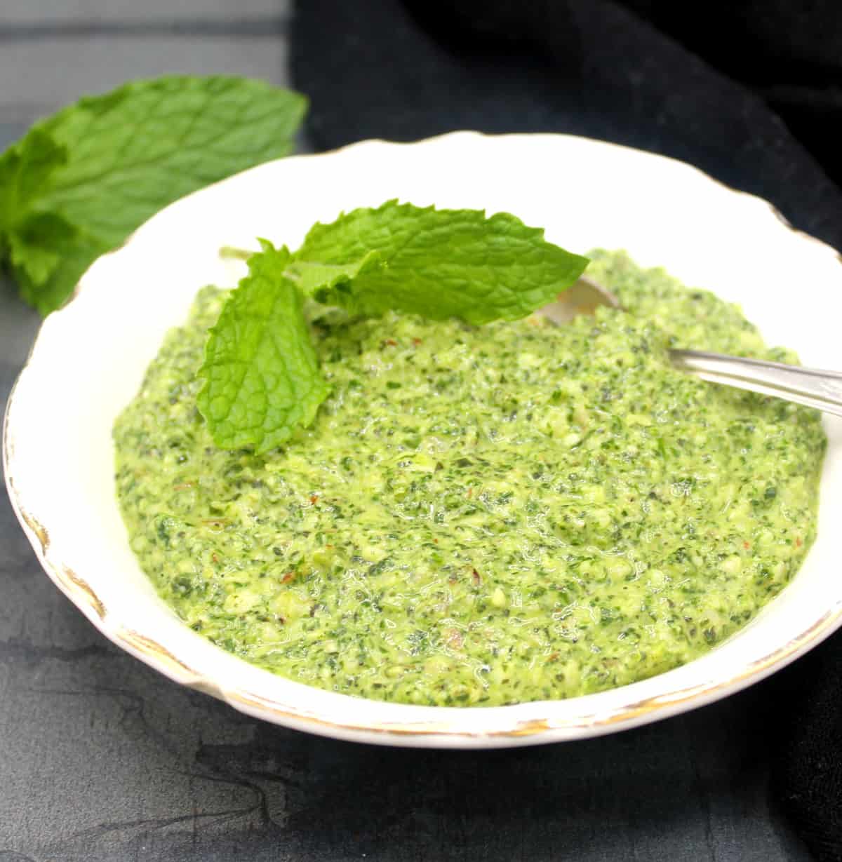 Vegan mint pesto in white bowl with a sprig of mint and spoon.