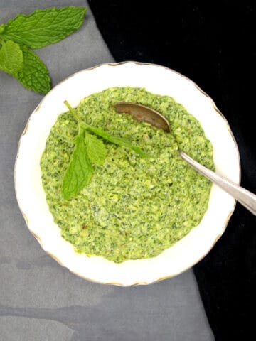 Vegan mint pesto in white bowl with spoon and a sprig of mint on the side.