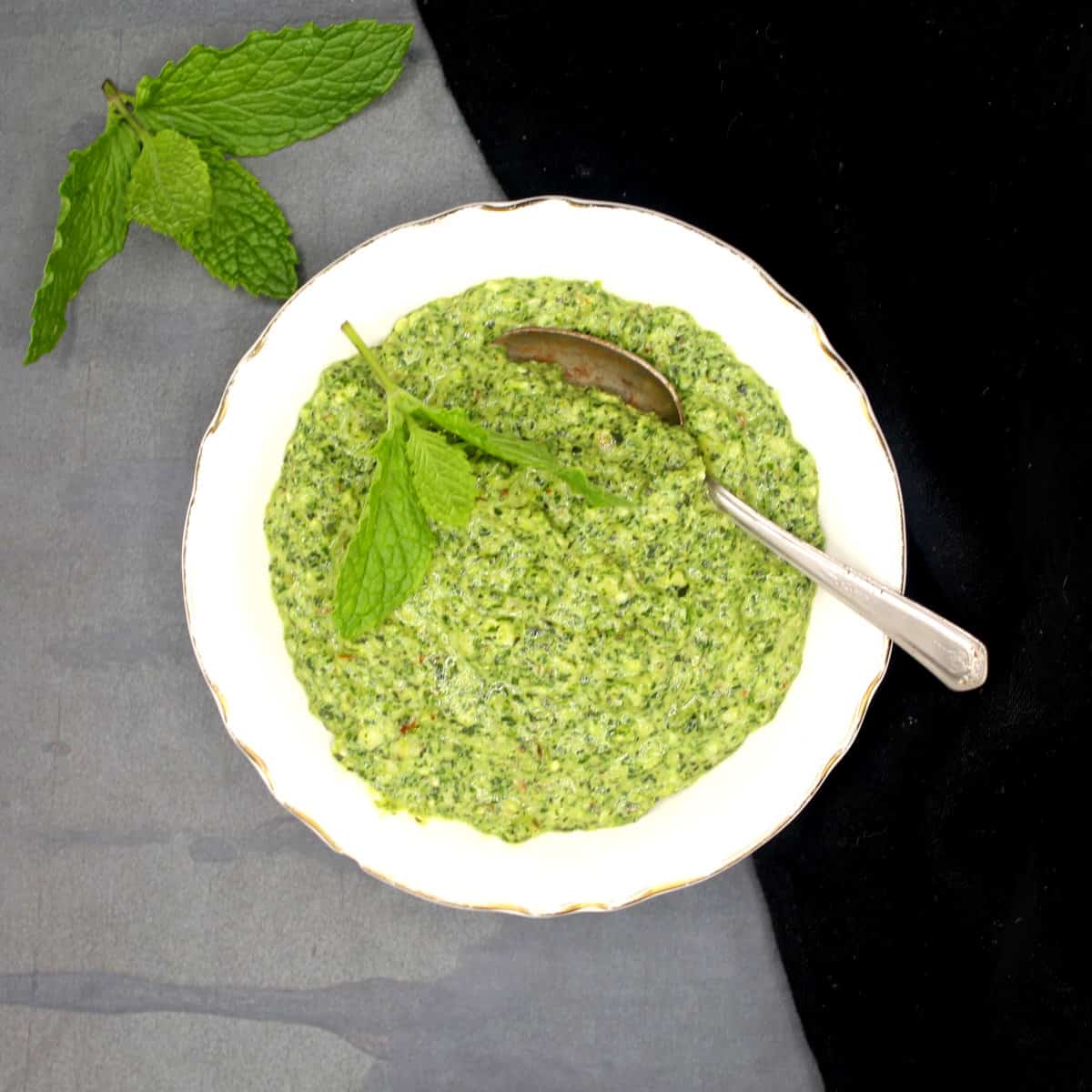 Vegan mint pesto in white bowl with spoon and a sprig of mint on the side.