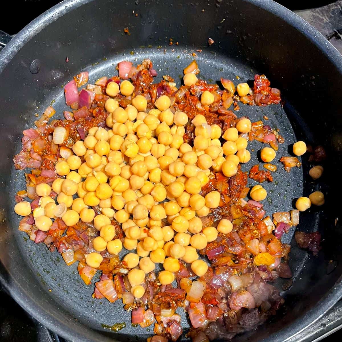 Chickpeas added to onions and tomato paste in saucepan for khoresh bademjan.