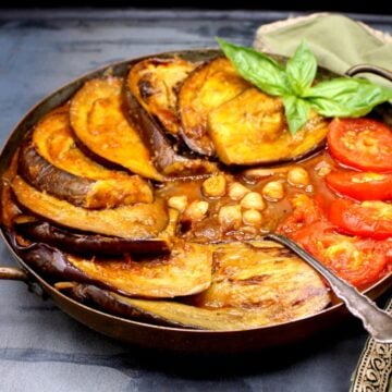 Persian Eggplant Stew Khoresh Bademjan in a copper pan with eggplant, tomatoes and a sprig of basil.
