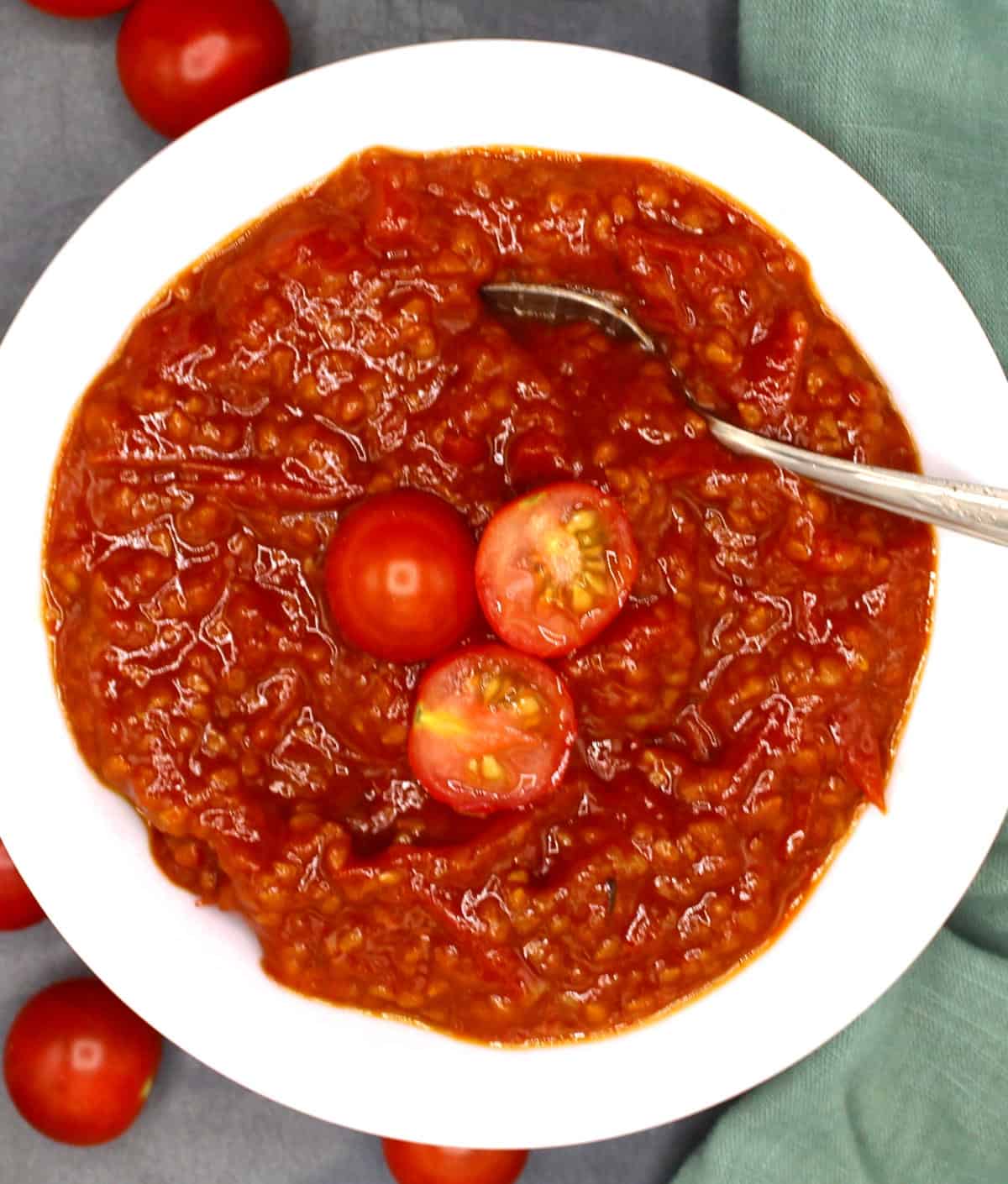 Tomato compote in white bowl with cherry tomatoes and spoon.