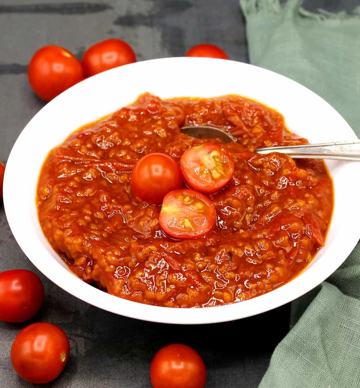 Tomato compote in white bowl with cherry tomatoes and spoon.