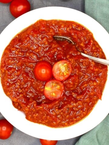 Tomato compote in white bowl with spoon and cherry tomatoes.