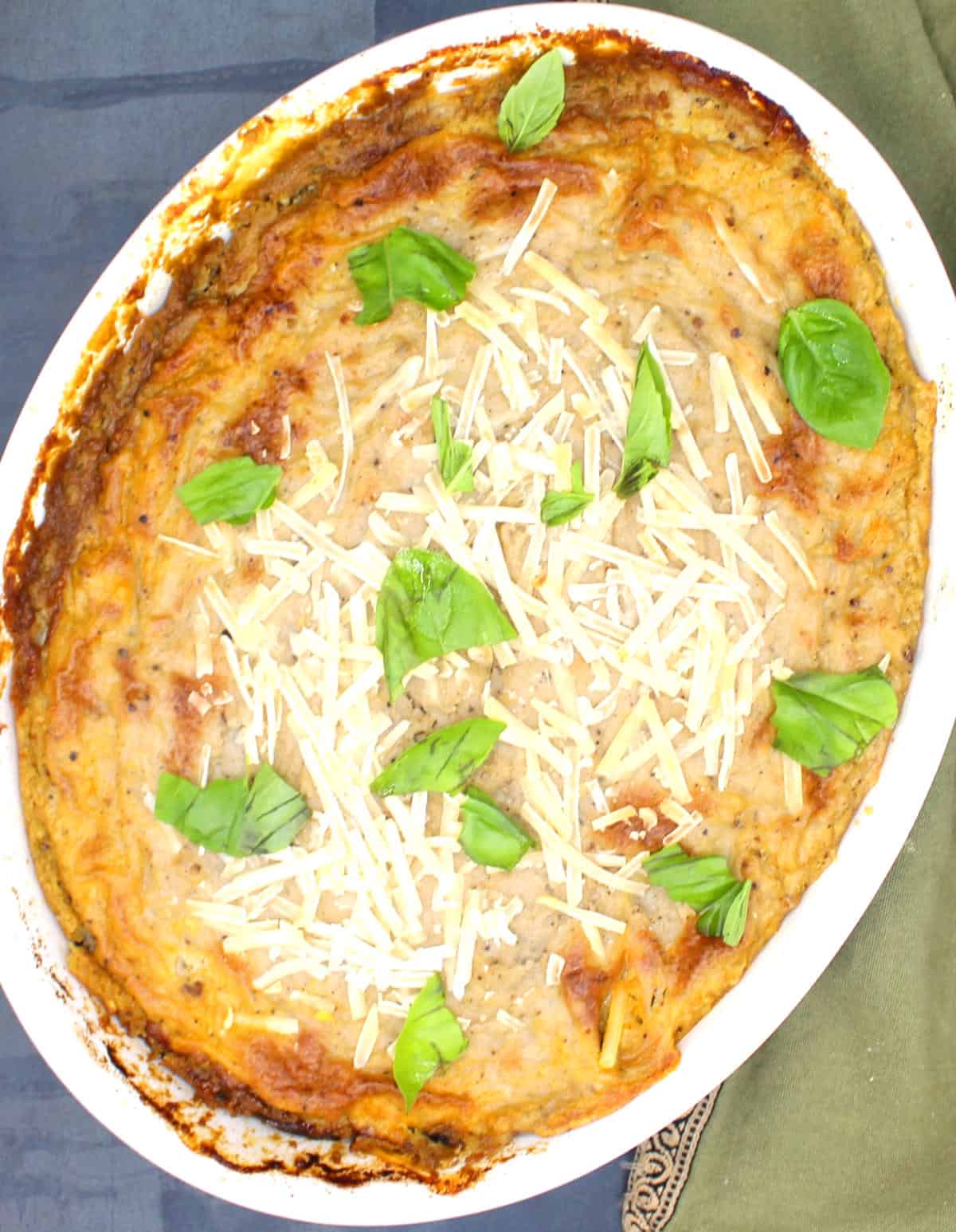 Baked vegan moussaka in oval baking dish with basil garnish.
