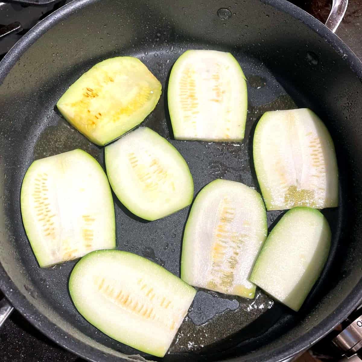 Zucchini slices frying in pan.
