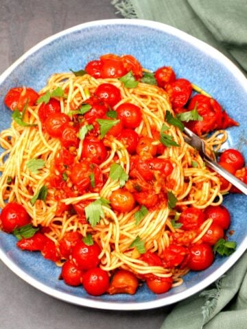 Cherry tomato pasta in bowl with fork and parsley garnish.