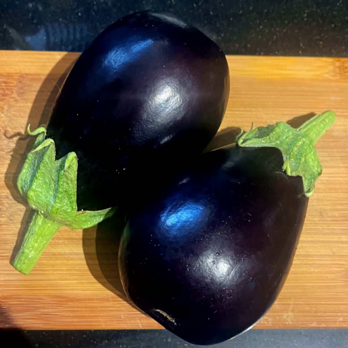 Two eggplants on chopping board.