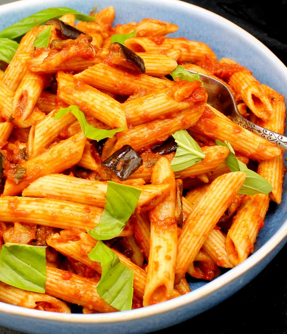 Pasta alla Norma in a blue bowl with basil.
