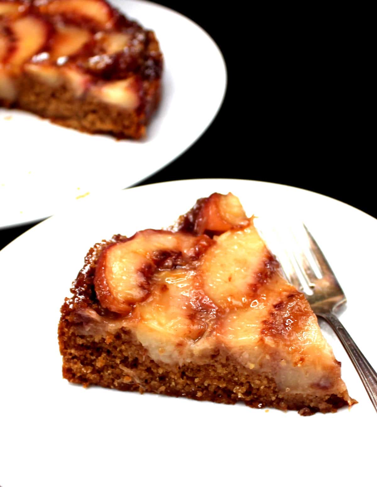 Slice of vegan peach upside down cake in white plate with fork.