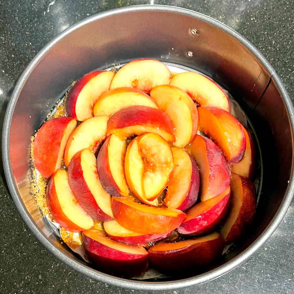 Peaches arranged in cake pan for upside-down peach cake.