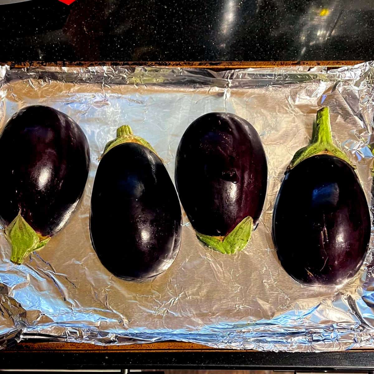 Eggplant halves on foil lined baking sheet for roasting.