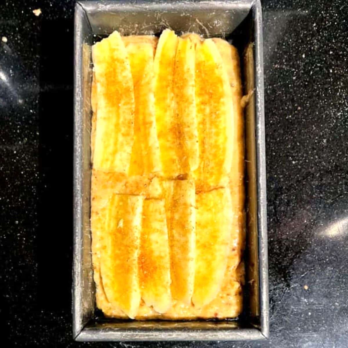 Vegan banana bread loaf in loaf pan before baking with banana slices on top.