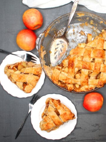 Vegan apple pie with slices of apple pie in white plates and forks and apples scattered around.