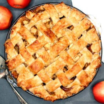 Vegan apple pie with lattice crust and apples scattered around.