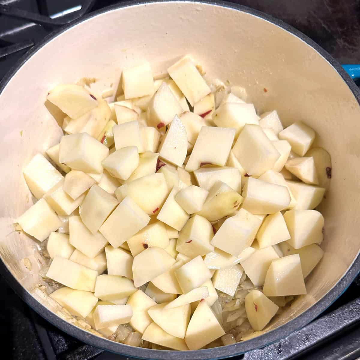 Potatoes added to pot with onions, garlic and rosemary for vegan potato soup.