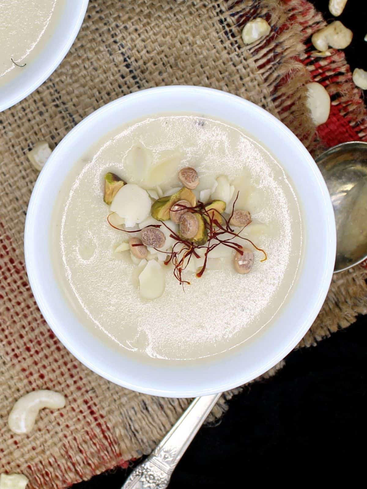 Vegan rabri in bowl with nuts and saffron garnish with cashews strewn around.