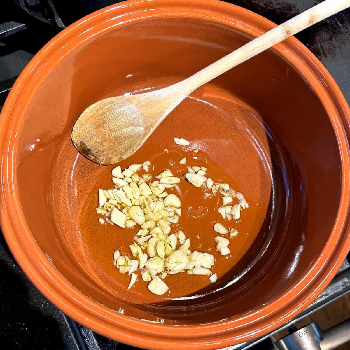 Garlic sauteing in olive oil in pot with wooden ladle.