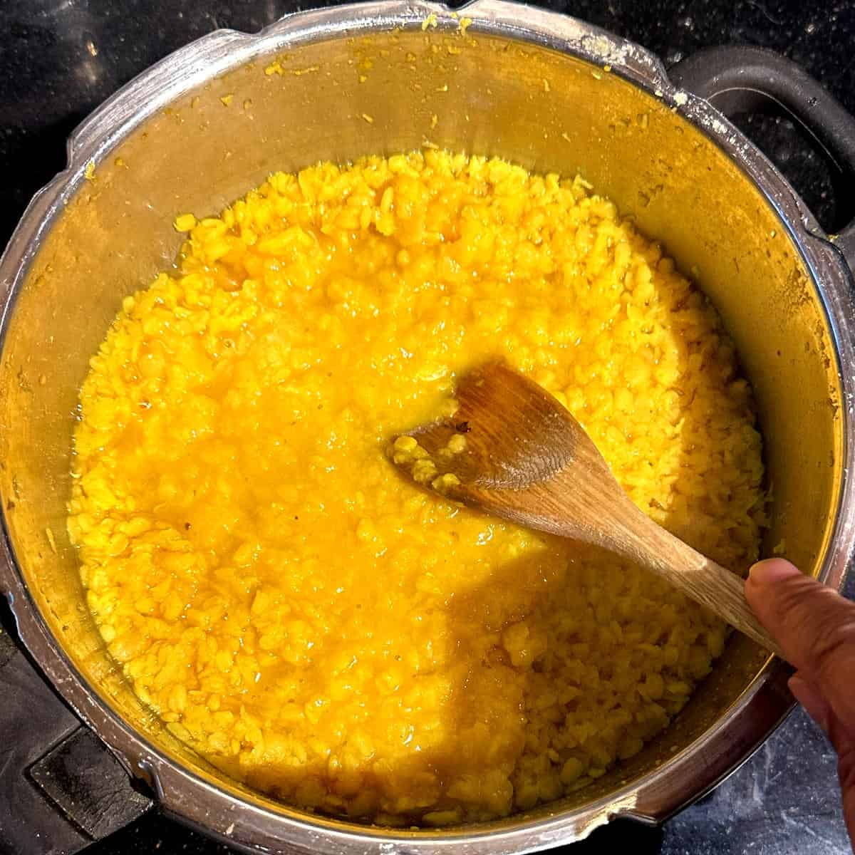 Mashing the cooked dal in pressure cooker with wooden spoon.