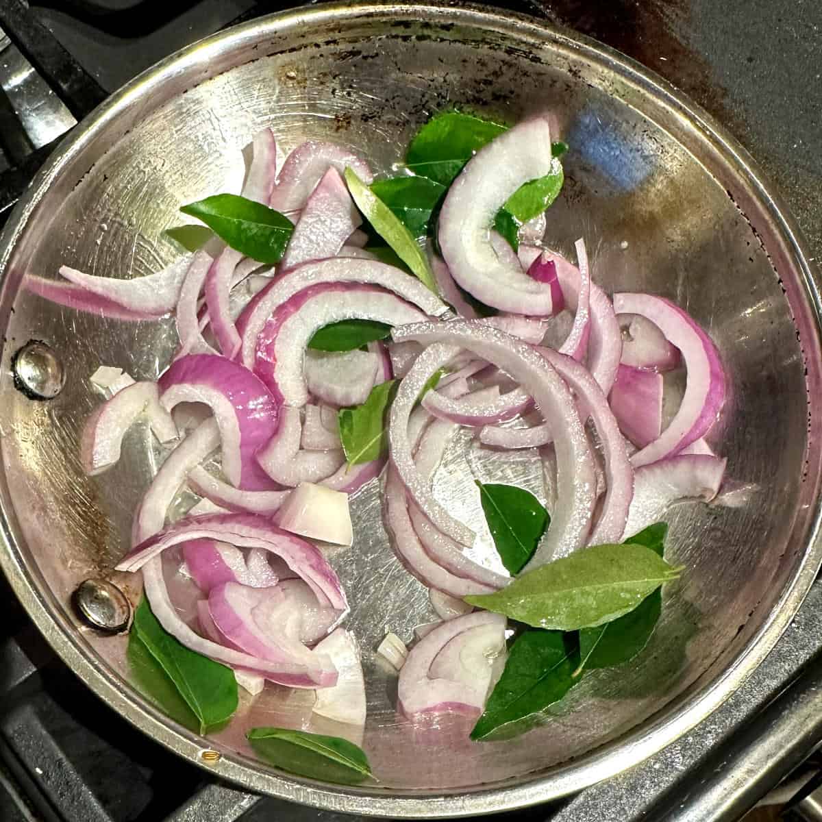 Onions and curry leaves in skillet for sambar masala.