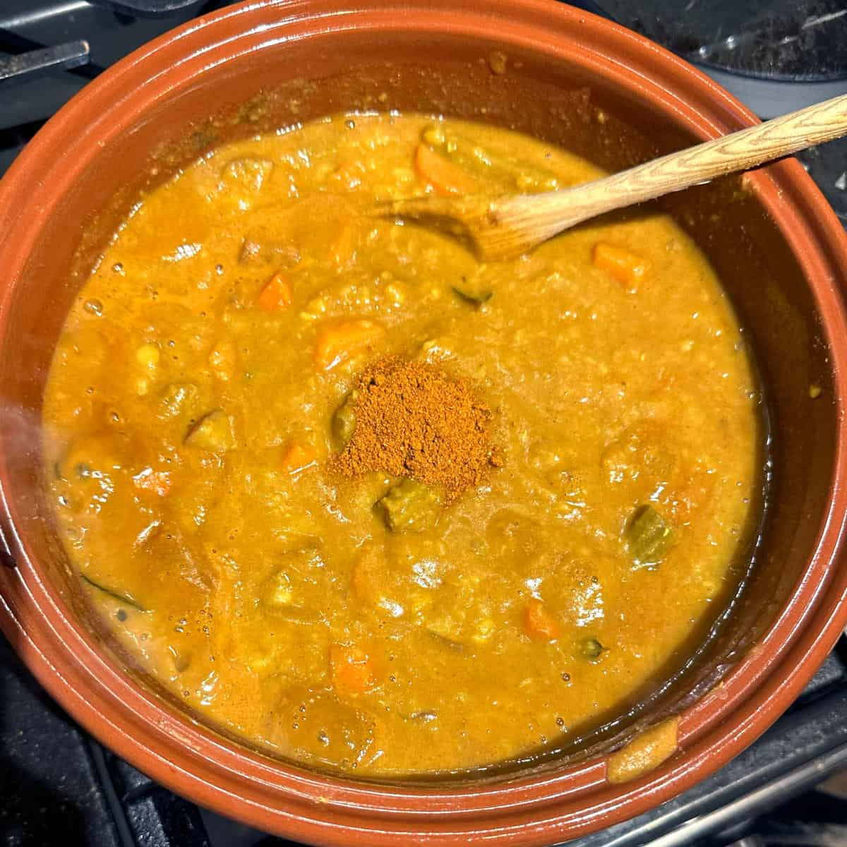 Sambar powder added to pot with wooden spoon.