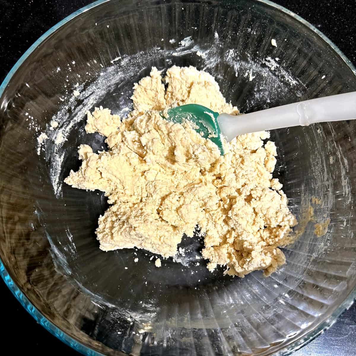 Dry and wet ingredients for vegan sable mixed in bowl with spatula.