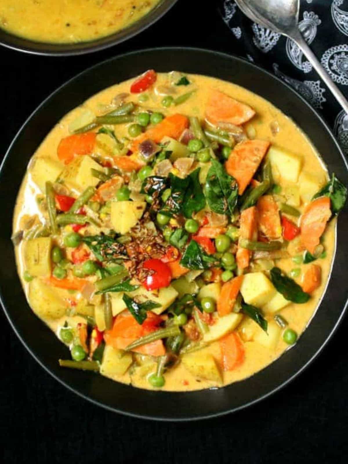 Vegetable korma in black bowl with curry leaves tempering.